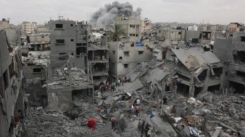 Rescatistas palestinos revisan el lugar de un bombardeo israelí sobre un edificio residencial en el vecindario de Shujaiyya, en la ciudad de Gaza, mientras el humo de otro ataque se eleva en el fondo, el 9 de abril de 2025. (AFP)