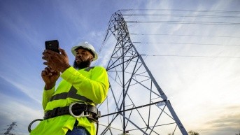 Fotografía sin fecha específica de toma cedida por T-Mobile que muestra a una persona observando su teléfono frente a una torre eléctrica en Estados Unidos. (T-Mobile / EFE)