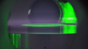 Una vista dentro de la cámara de vacío del laboratorio, donde las partículas coloidales están suspendidas en un disco plano, iluminado por la luz verde de un láser, para estudiar el plasma polvoriento. (Internet)