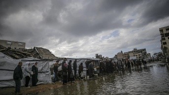 CIUDAD DE GAZA, 26 de noviembre, palestinos caminan a través de un charco cerca de tiendas de campaña improvisadas durante un día lluvioso en la Ciudad de Gaza. (EFE)