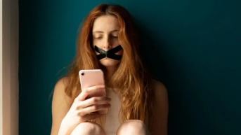 Mujer con su smartphone y cinta en la boca. (Getty Images)