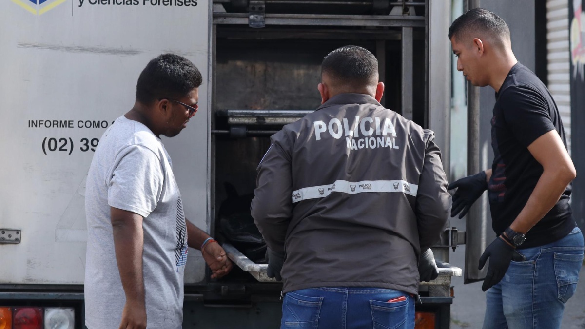 Imagen de un policía llevando un cuerpo de un hombre asesinado al interior de un carro de Medicina Legal, en Durán. (César Muñoz/API)