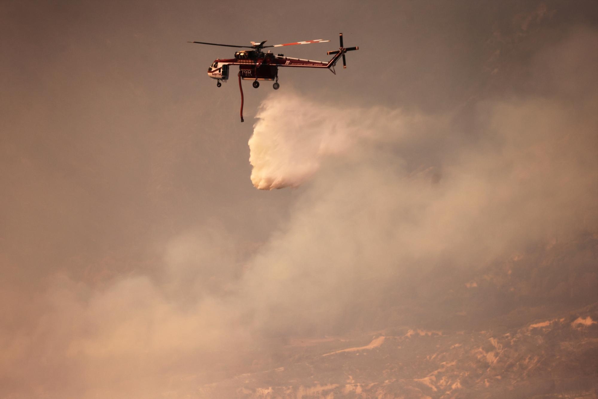 Water is dropped from a helicopter as the Line Fire burns over 43,000 acres near Big Bear Lake in San Bernardino County, California, September 30, 2024. (Photo by David SWANSON / AFP) (DAVID SWANSON / AFP)