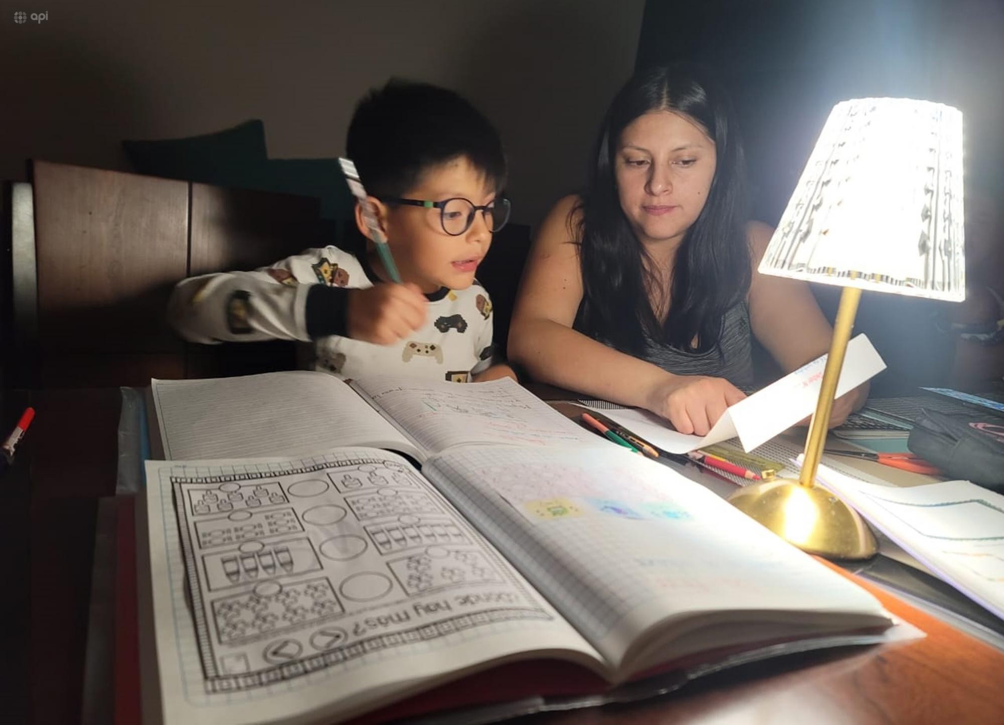 Imagen de un niño haciendo deberes con su madre, con una lámpara, en medio de la oscuridad, ante los apagones. (API)