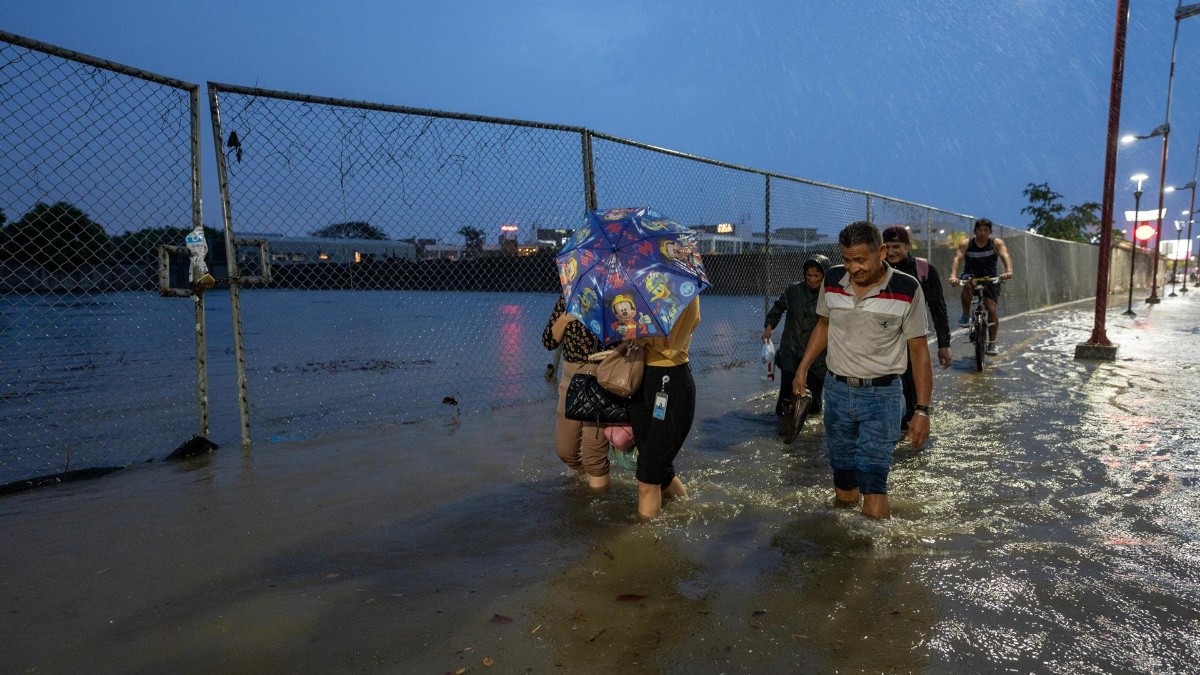 Foto del pasado 20 de febrero, en la que se registró a un grupo de personas al caminar por una vía inundada. (EFE)
